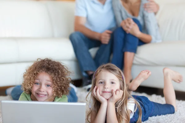 Crianças bonitos usando um laptop enquanto seus pais estão assistindo — Fotografia de Stock