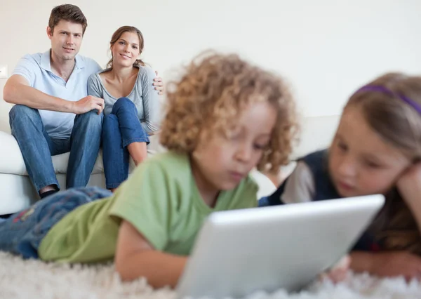 Enfants mignons à l'aide d'un ordinateur tablette tandis que leurs parents heureux — Photo