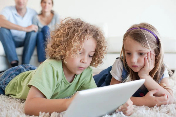 Niños serios usando una tableta mientras sus padres felices —  Fotos de Stock