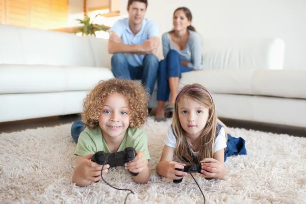 Niños jugando videojuegos mientras sus padres están viendo — Foto de Stock