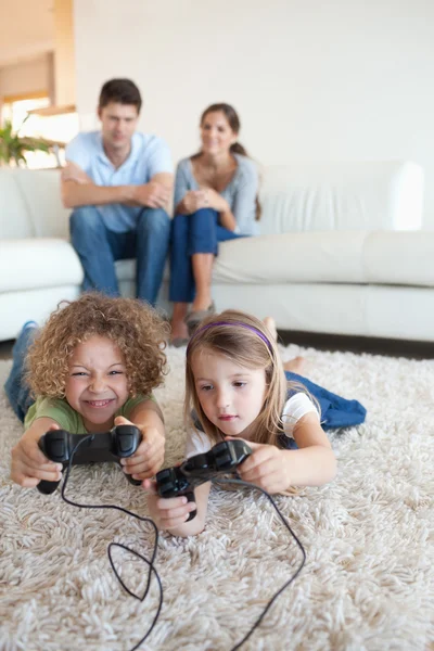 Retrato de niños jugando videojuegos mientras sus padres son — Foto de Stock