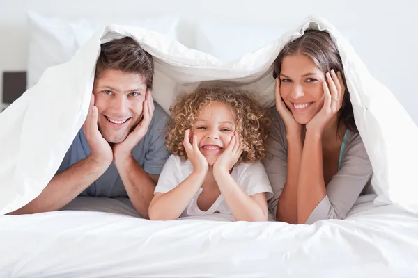 Familia feliz posando bajo un edredón — Foto de Stock