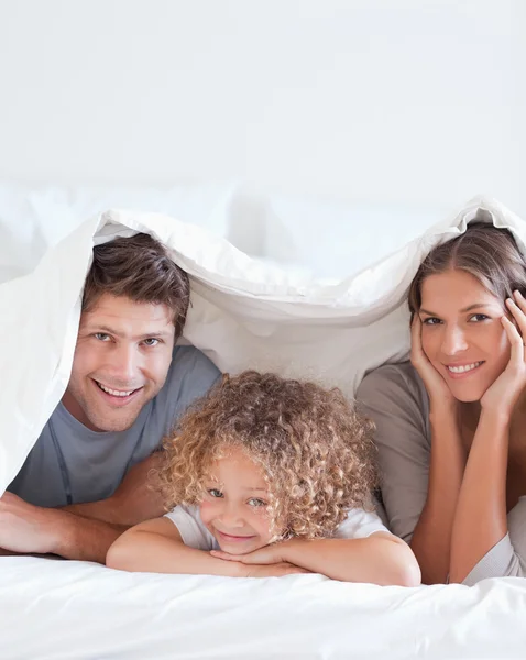 Família sorridente deitada na cama — Fotografia de Stock