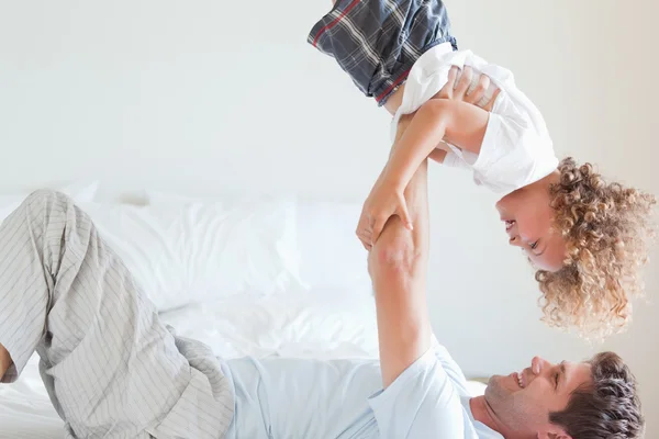 Вид сбоку отца, поднимающего ребенка на кровать — стоковое фото