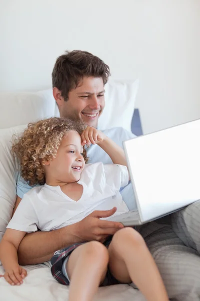 微笑的父亲和孩子在床上用的笔记本电脑 — 图库照片