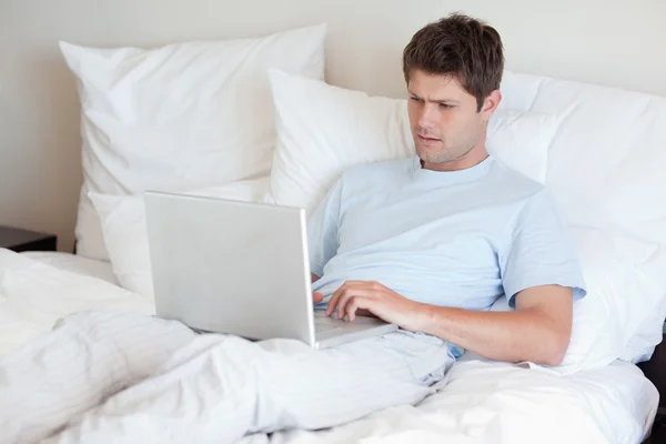 男子躺在床上用的笔记本电脑 — 图库照片