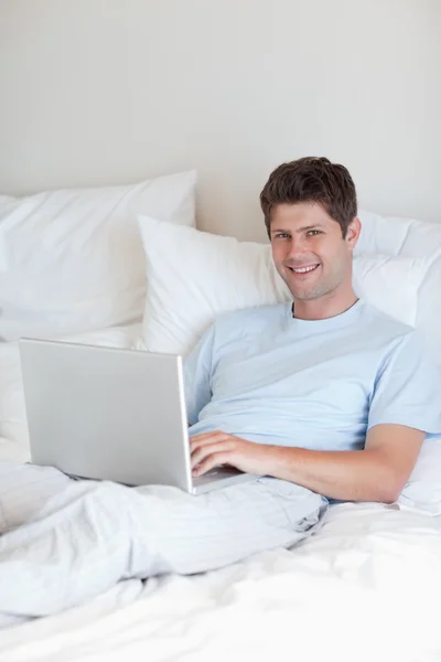 Homem sorridente deitado na cama com caderno — Fotografia de Stock