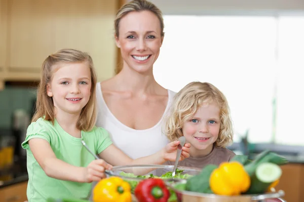 Smiling woman with her children preparing salad — Stock Photo, Image