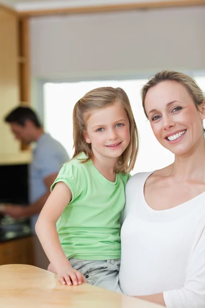Mother holding her daughter with father in the background — Stock Photo, Image