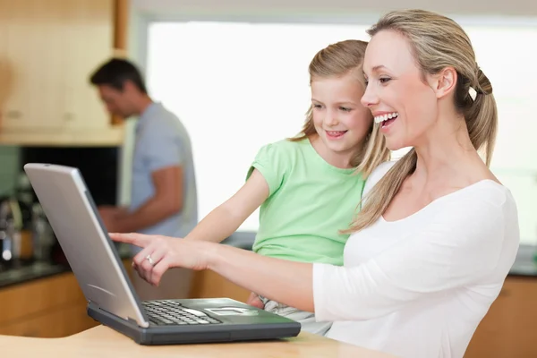 Happy mother and daughter using laptop with father in the backgr — Stock Photo, Image