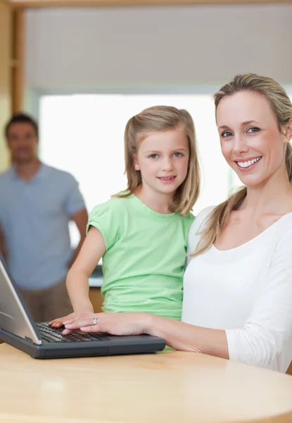 Anne ve kızı babası arka planda olan dizüstü bilgisayar kullanarak — Stok fotoğraf