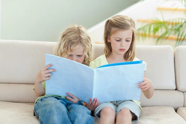 Siblings reading magazine on the sofa — Stock Photo, Image