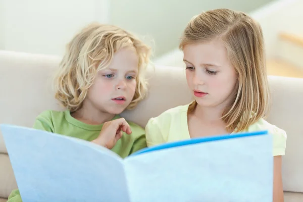 Siblings reading magazine on the couch — Stock Photo, Image