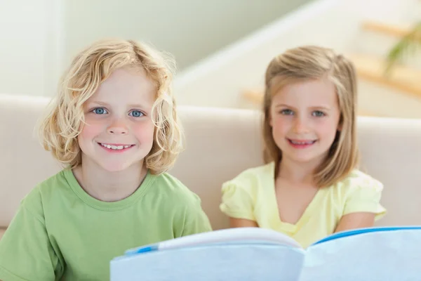 Siblings reading booklet on the sofa — Stock Photo, Image