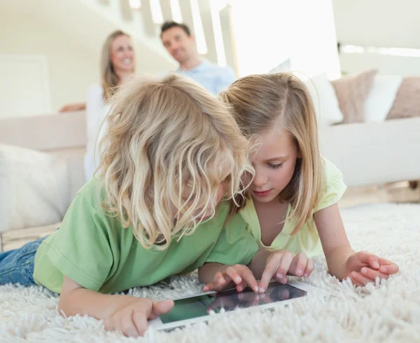 Geschwister auf dem Boden mit Tablet und Eltern im Rücken — Stockfoto