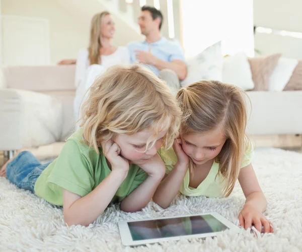 Children on the floor with tablet and parents behind them — Stock Photo, Image