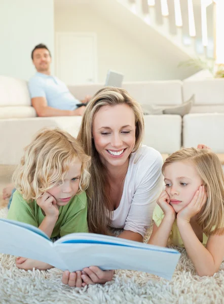 Mother reading magazine with her children on the floor — Stock Photo, Image