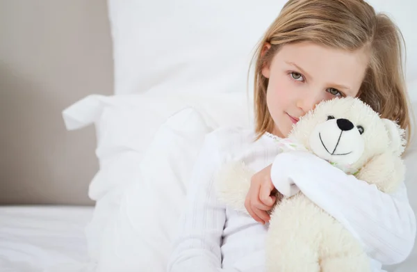 Meisje met haar teddy zittend op het bed — Stockfoto
