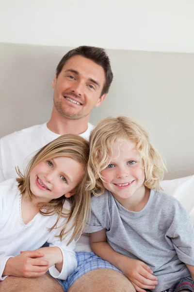 Улыбающийся отец сидит на кровати со своими детьми — стоковое фото
