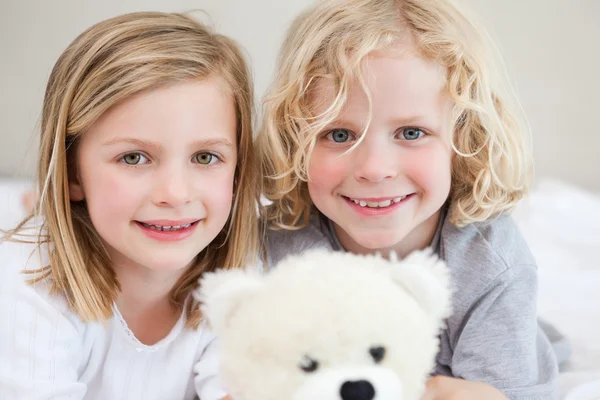 Siblings lying on the bed with their teddy — Stock Photo, Image