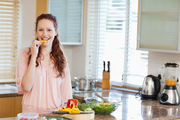 Woman nibbling bell pepper while preparing salad — Stock Photo, Image
