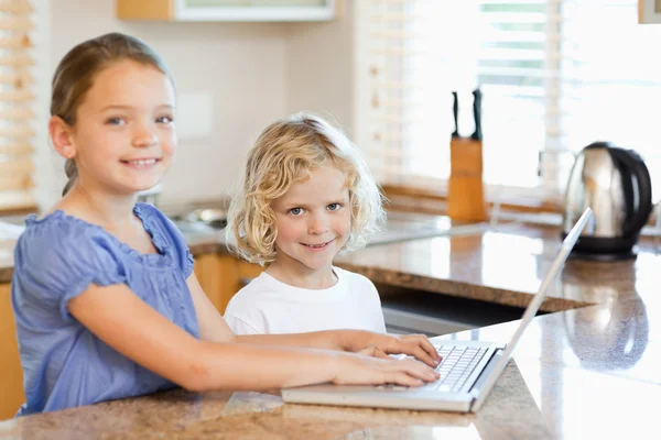 Irmãos sorridentes no laptop na cozinha — Fotografia de Stock