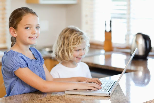 Siblings with laptop behind the kitchen counter — Stock Photo, Image