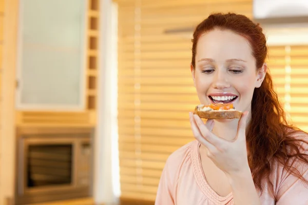 Woman eating a slice of bread in the kitchen — Stock Photo, Image