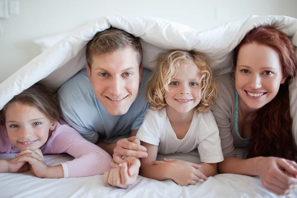 Lächelnde Familie unter Bettdecke — Stockfoto