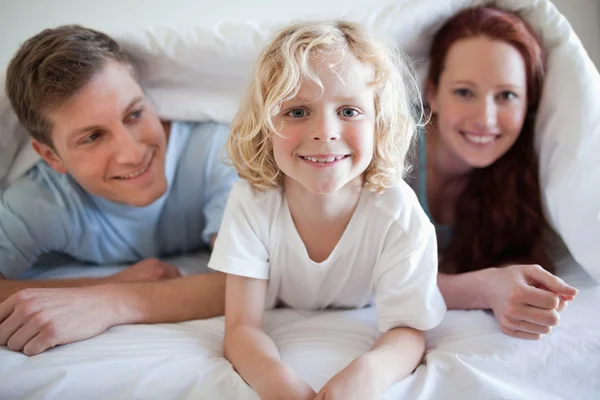 Lächelnder Junge unter der Decke mit seinen Eltern — Stockfoto