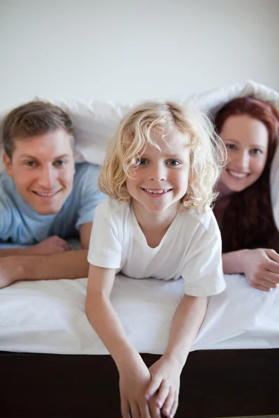 Χαρούμενα αγόρι κάτω από το κάλυμμα του κρεβατιού με τους γονείς του — Φωτογραφία Αρχείου