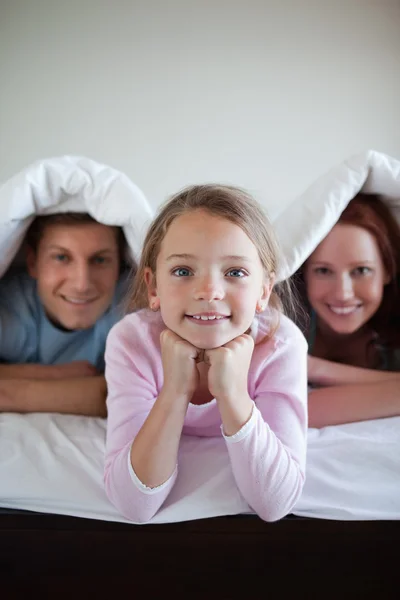 Sorrindo menina sob a cama cobrir com seus pais — Fotografia de Stock