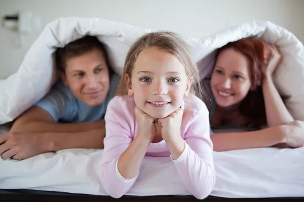 Chica alegre bajo la cama cubierta con los padres —  Fotos de Stock
