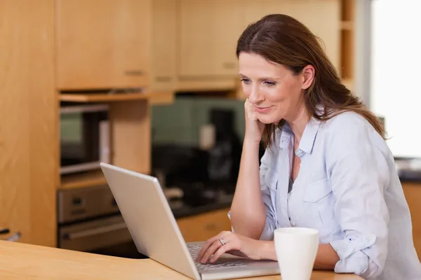 Mulher na cozinha olhando para seu laptop — Fotografia de Stock