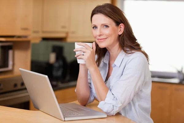 Kvinna dricker kaffe medan på laptop — Stockfoto