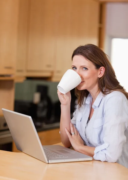 Женщина делает глоток кофе рядом с ноутбуком — стоковое фото