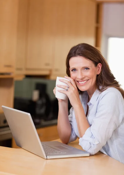 Женщина с чашкой рядом с ноутбуком — стоковое фото