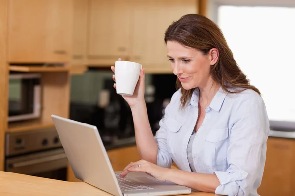Женщина пьет чай на ноутбуке — стоковое фото