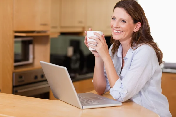 Vrouw met cup en laptop in de keuken — Stockfoto
