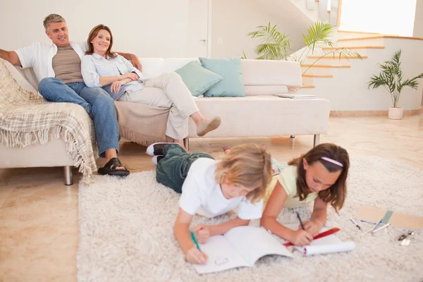 Niños haciendo deberes con los padres detrás de ellos —  Fotos de Stock