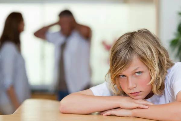 Triest uitziende jongen met ruzie ouders achter hem — Stockfoto