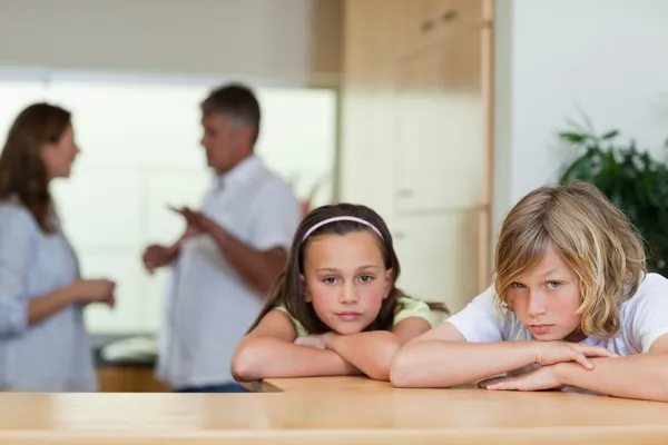 Traurig aussehende Geschwister mit kämpfenden Eltern im Rücken — Stockfoto