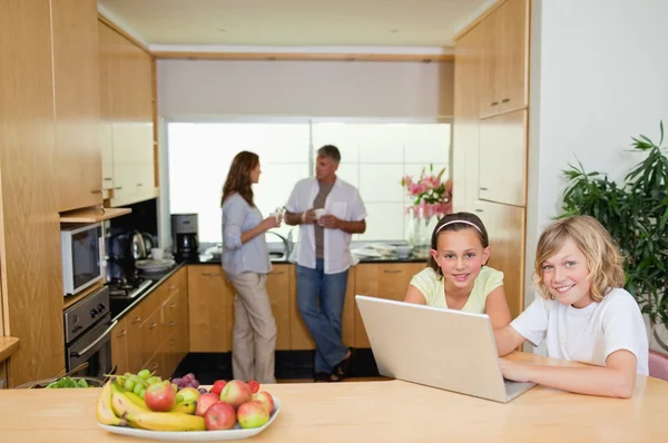 Children with notebook in the kitchen and parents behind them — Stock Photo, Image