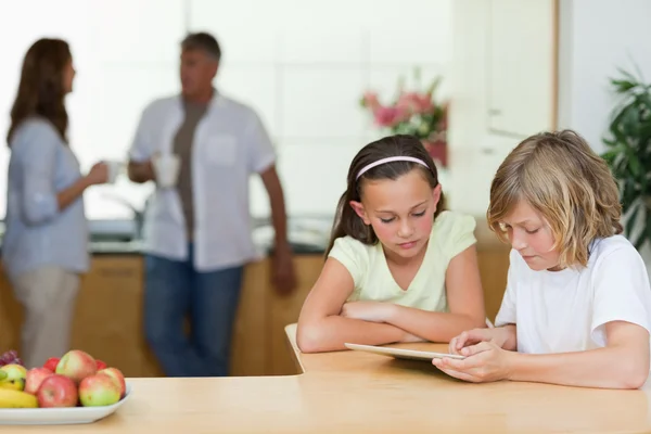 Kinder mit Tablet in der Küche, Eltern im Hintergrund — Stockfoto