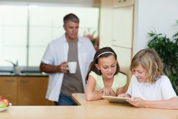 Niños usando tableta en la cocina con padre detrás de ellos —  Fotos de Stock