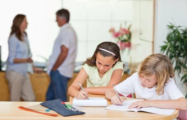 Frères et sœurs faisant leurs devoirs avec leurs parents derrière eux — Photo