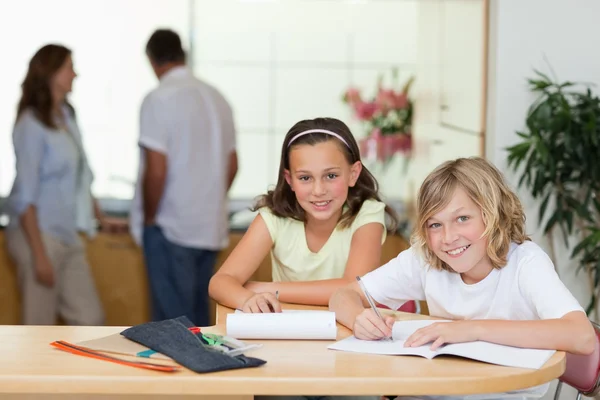 Sourozenci dělat domácí úkoly se svými rodiči za nimi — Stock fotografie