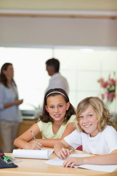 Crianças fazendo lição de casa com seus pais atrás deles — Fotografia de Stock