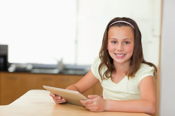 Menina sorridente com tablet na mesa da cozinha — Fotografia de Stock