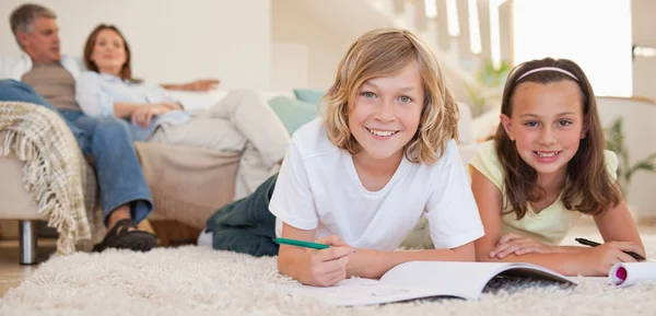 Broers en zussen doen hun huiswerk op de verdieping met ouders achter t — Stockfoto